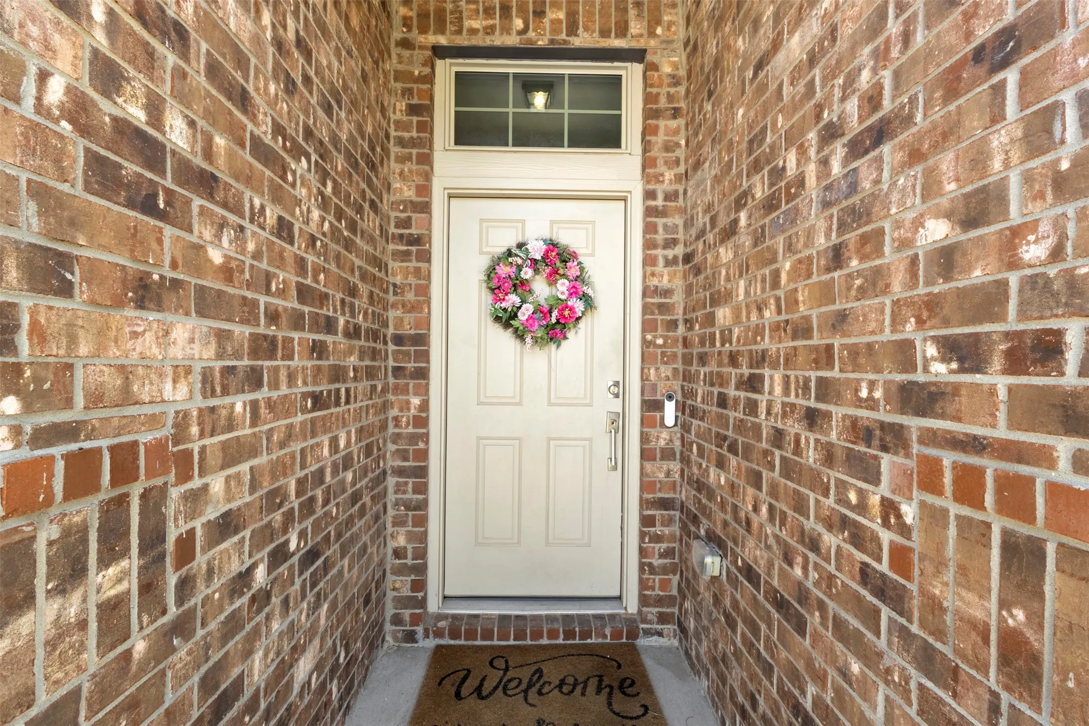 Recessed entry featuring brick walls, an overhead transom window, and an off-white entry door