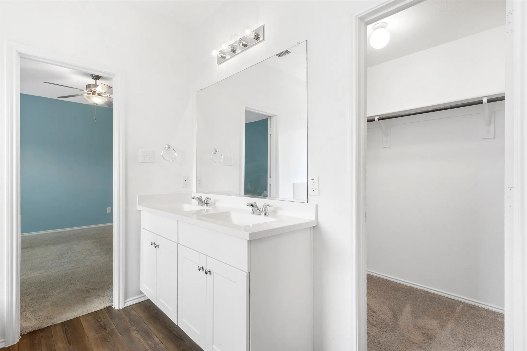 Dual vanity with white cabinetry, wood-finish flooring, and a mirrored wall