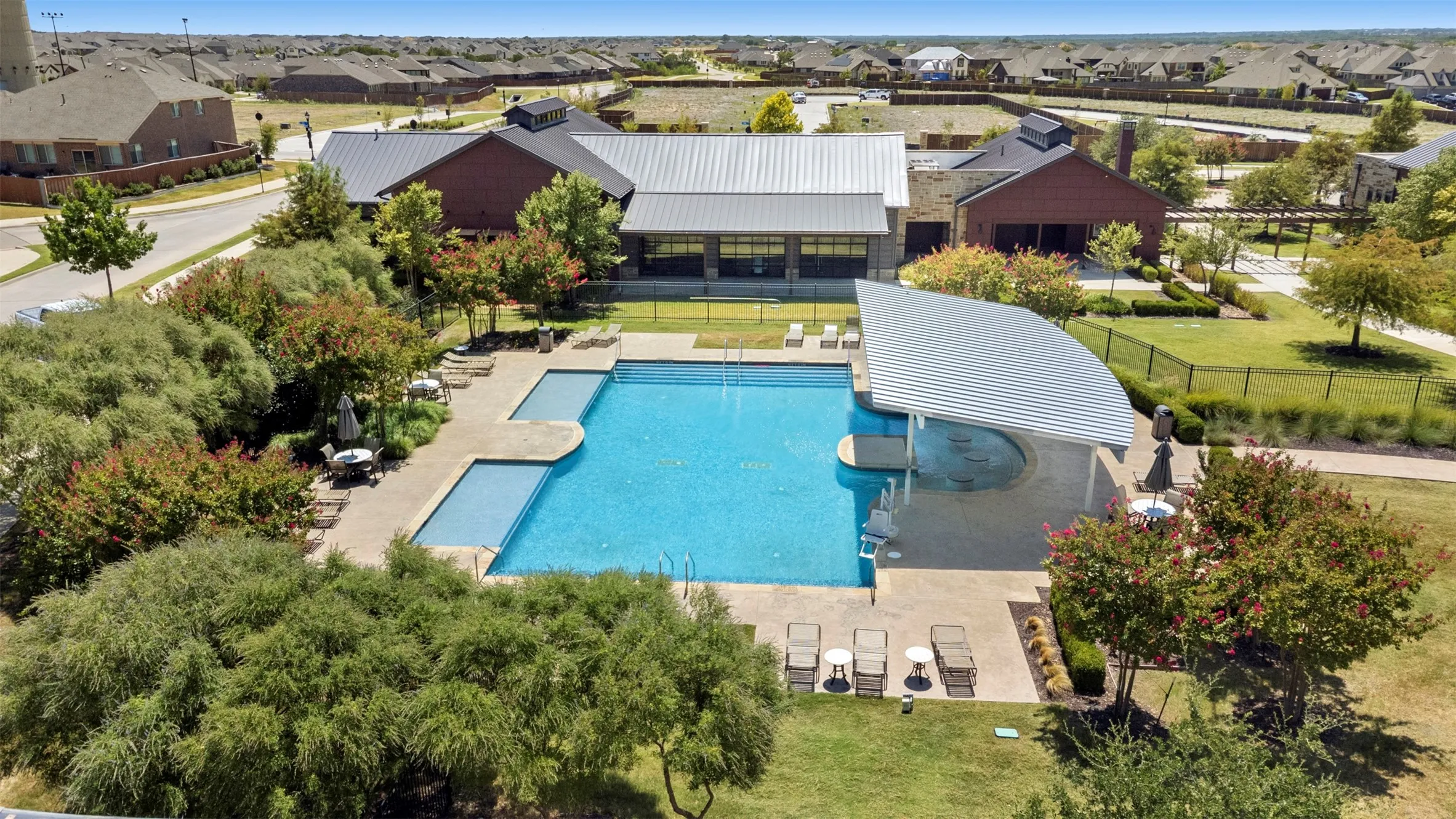 Expansive community pool with an integrated spa, shaded swim-up bar, surrounding paved deck, and adjacent green spaces