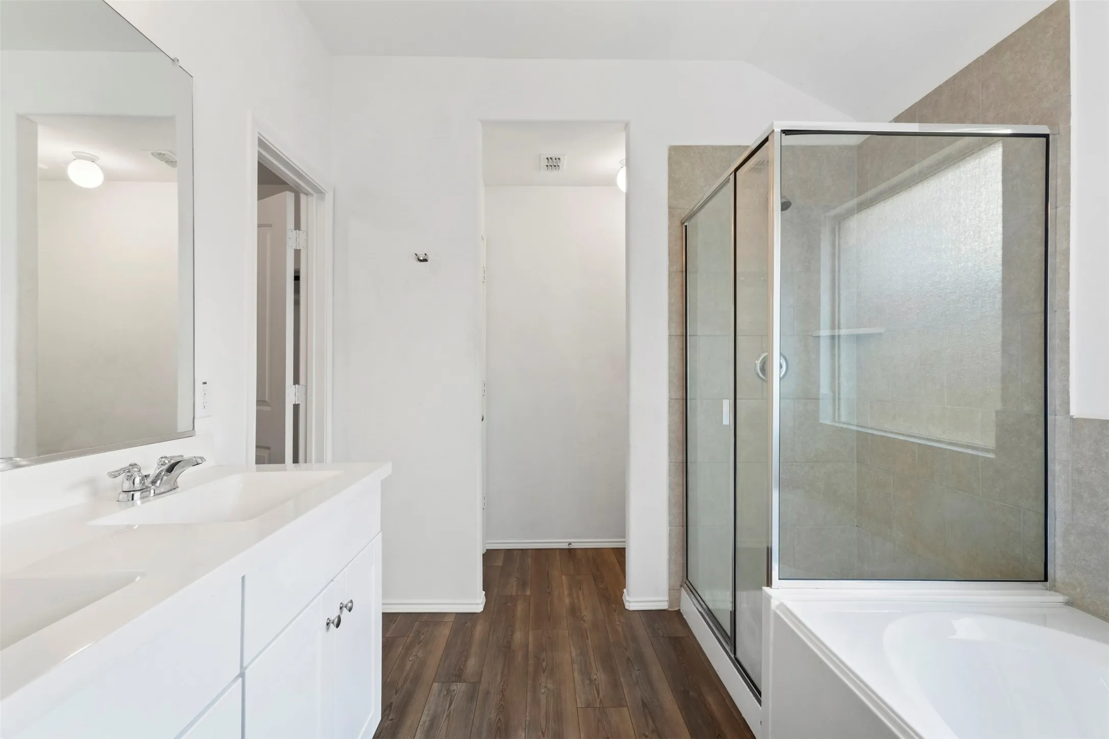 Dual sink vanity with white cabinetry, wood-finish flooring, glass-enclosed shower, and built-in​​‌​​​​‌​​‌‌​‌‌​​​‌‌​‌​‌​‌​​​‌​​ bathtub