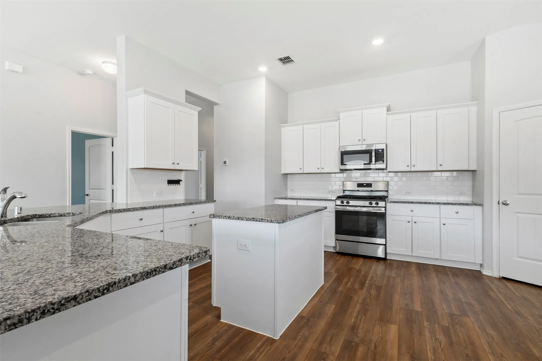 Kitchen featuring wood-finish flooring, white cabinetry, granite countertops, and stainless steel appliances