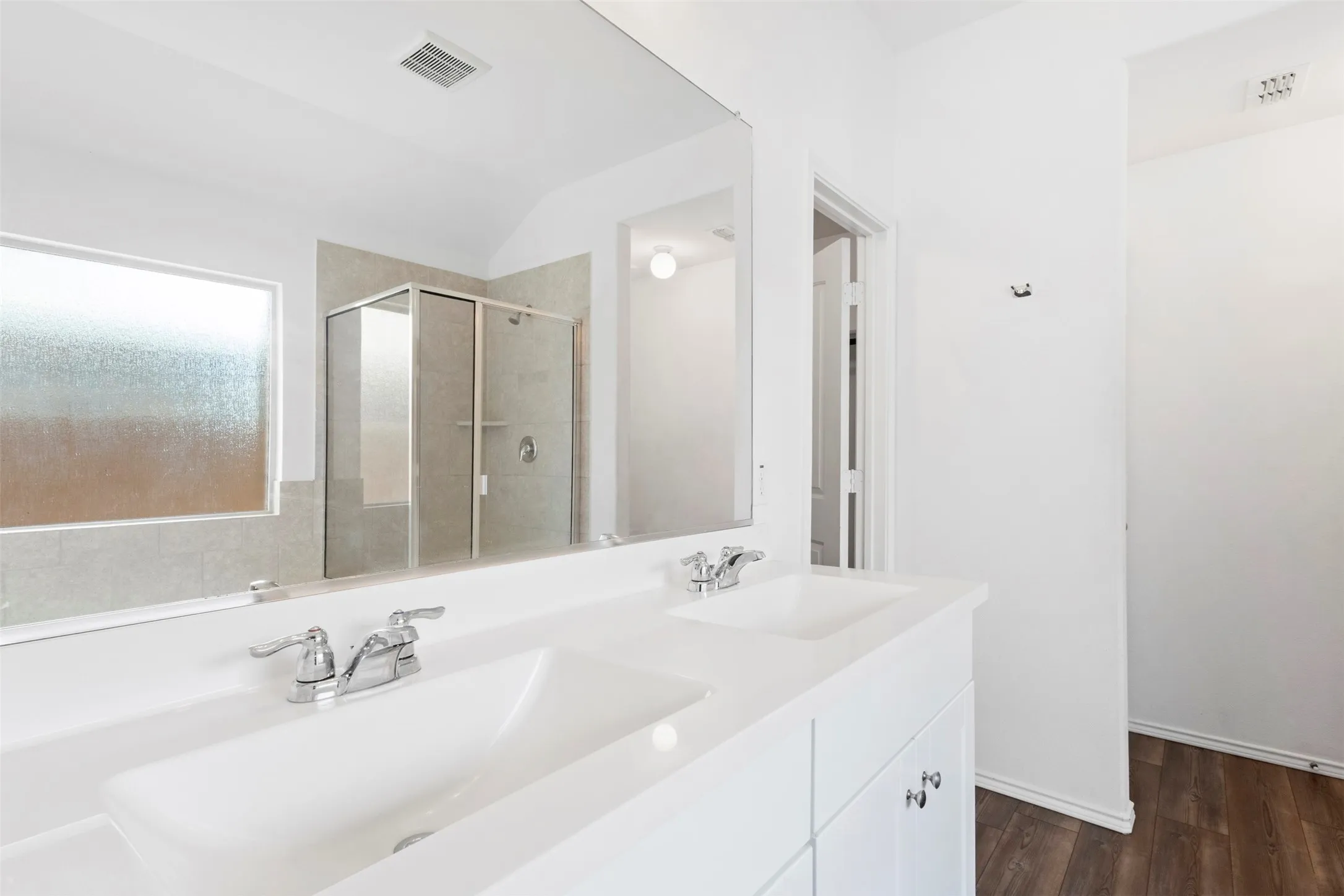 Double vanity with integrated sinks, chrome fixtures, built-in cabinetry, large mirror, and wood-finish flooring