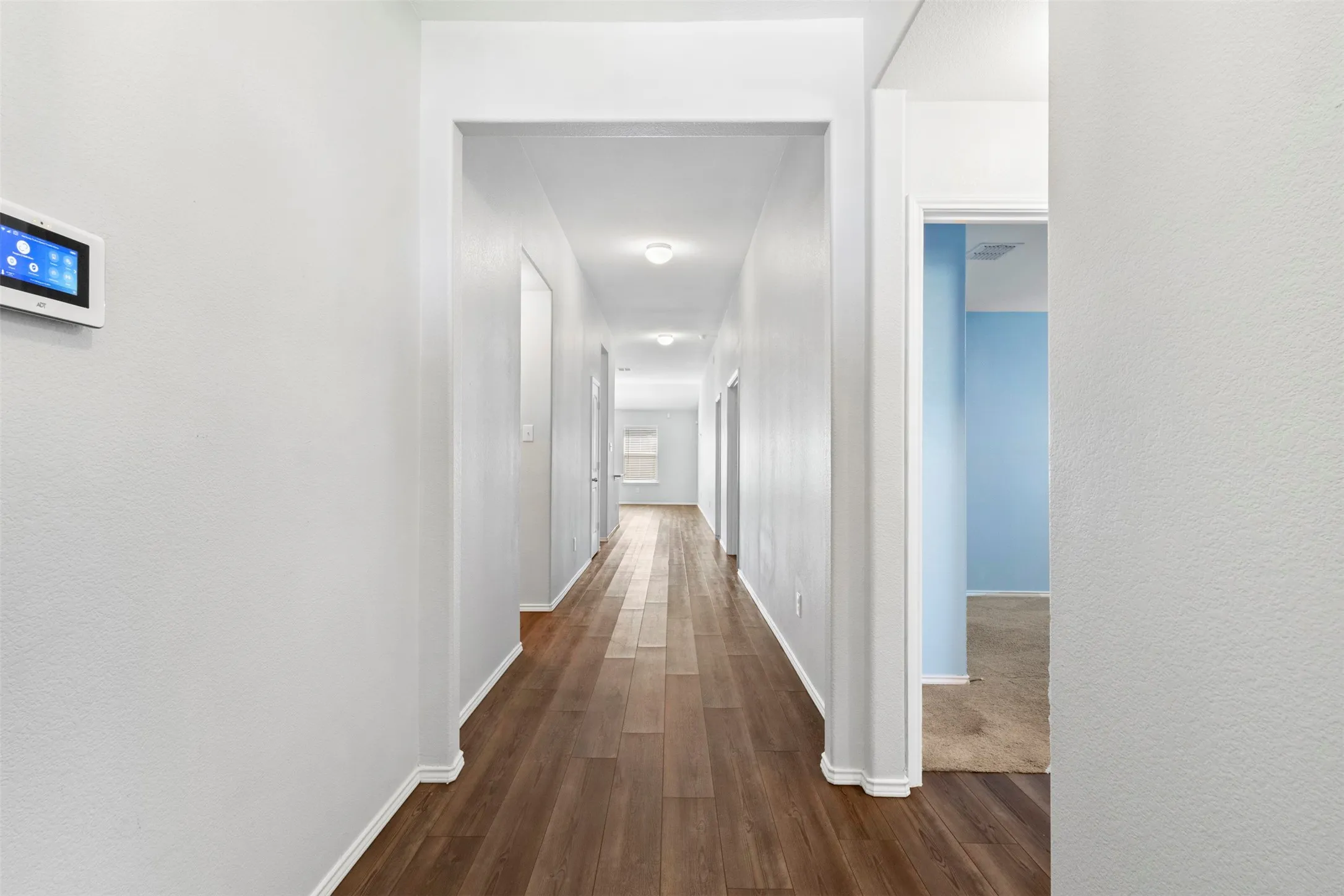 Long corridor with wood-finish flooring, white walls, and recessed lighting