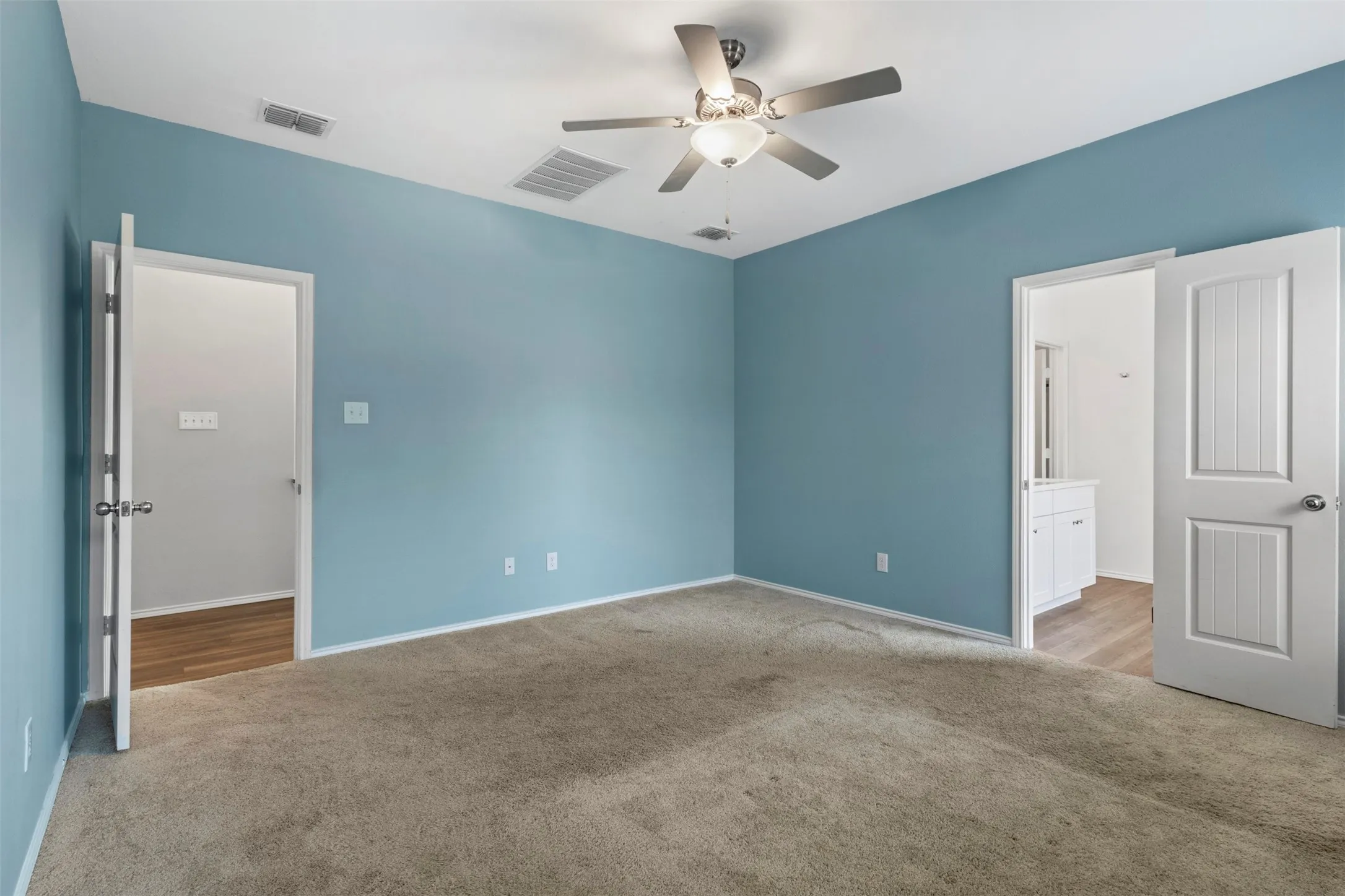 Spacious room featuring neutral carpeting, light blue walls, and a ceiling fan with integrated lighting