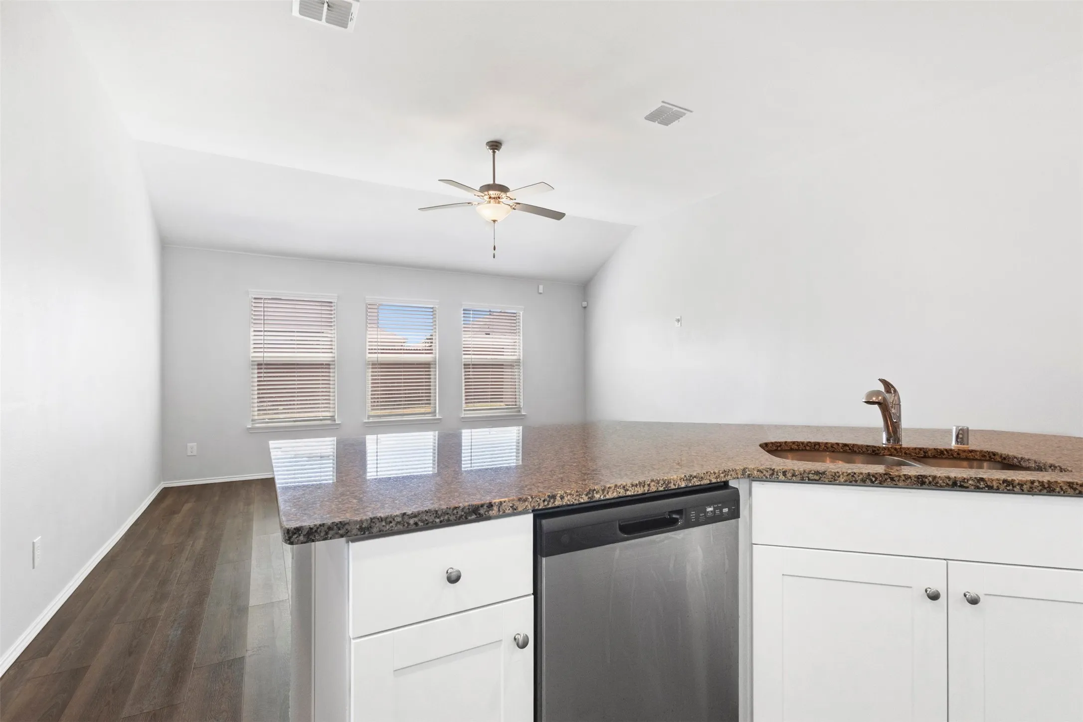Kitchen island featuring a granite countertop, undermount sink with a bronze-finish faucet, and stainless steel dishwasher