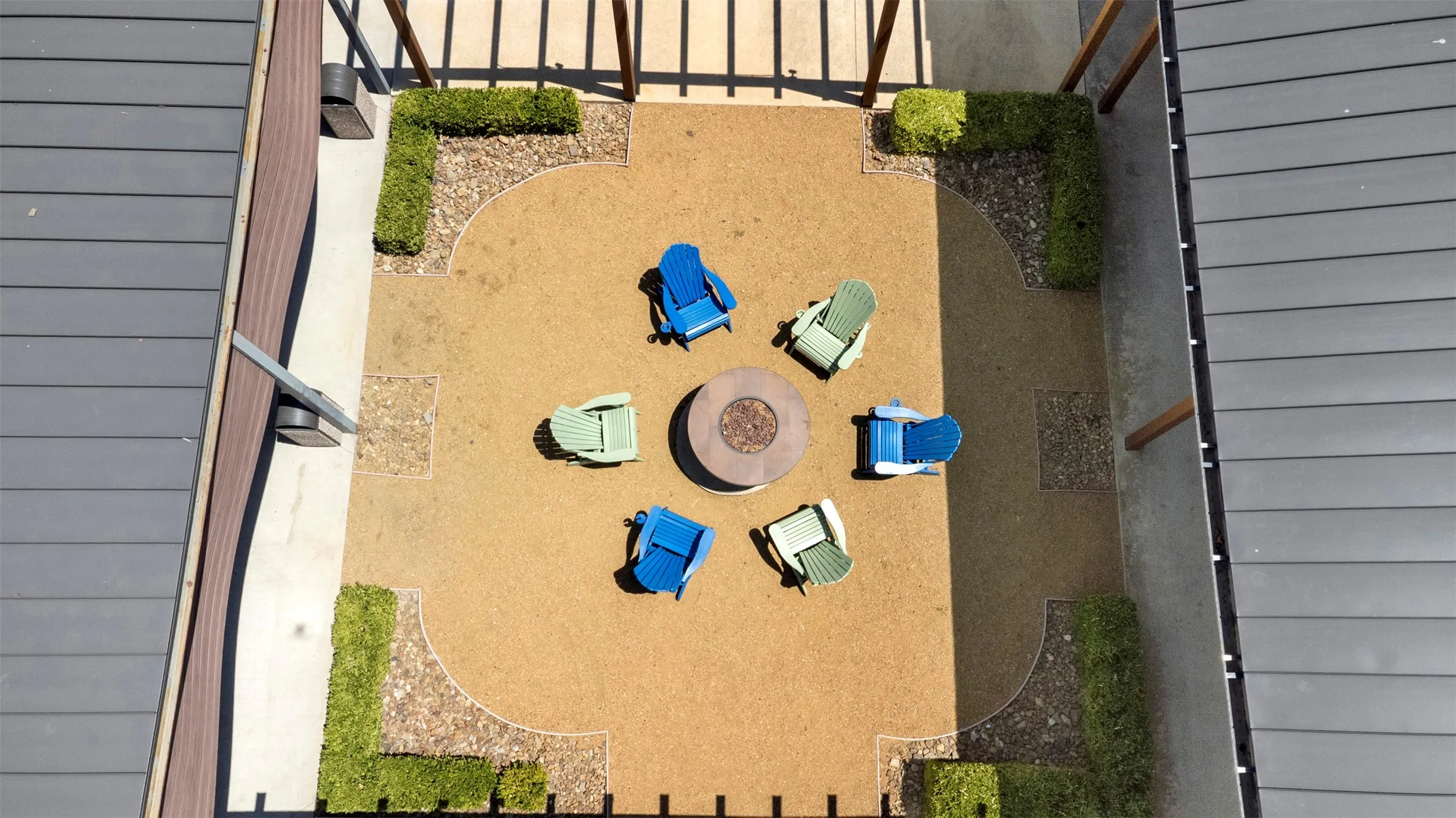 Central courtyard featuring a circular fire pit, surrounding gravel and concrete hardscaping, and structured landscaping with low hedges