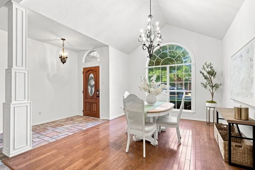 Vaulted ceiling, arched window, wood-finish flooring, decorative column, and solid wood entry door with oval glass insert