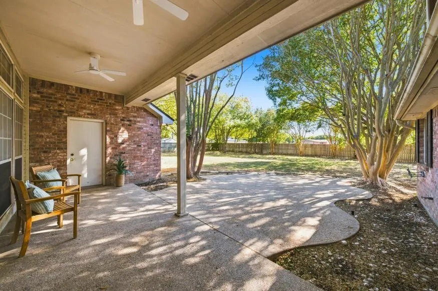 Covered patio with dual ceiling fans, extended concrete hardscaping, brick exterior, and a spacious grassy yard