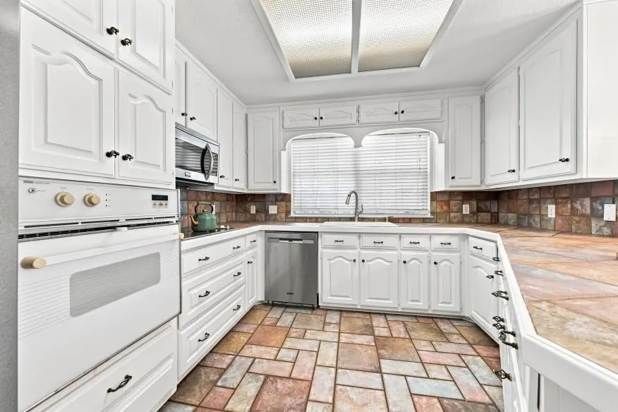 White cabinetry, stainless steel dishwasher, integrated microwave, built-in oven, and a tiled backsplash