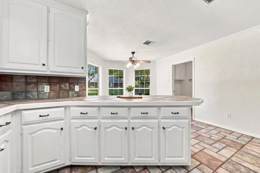 White cabinetry with dark hardware, multicolored tile backsplash, and a breakfast bar