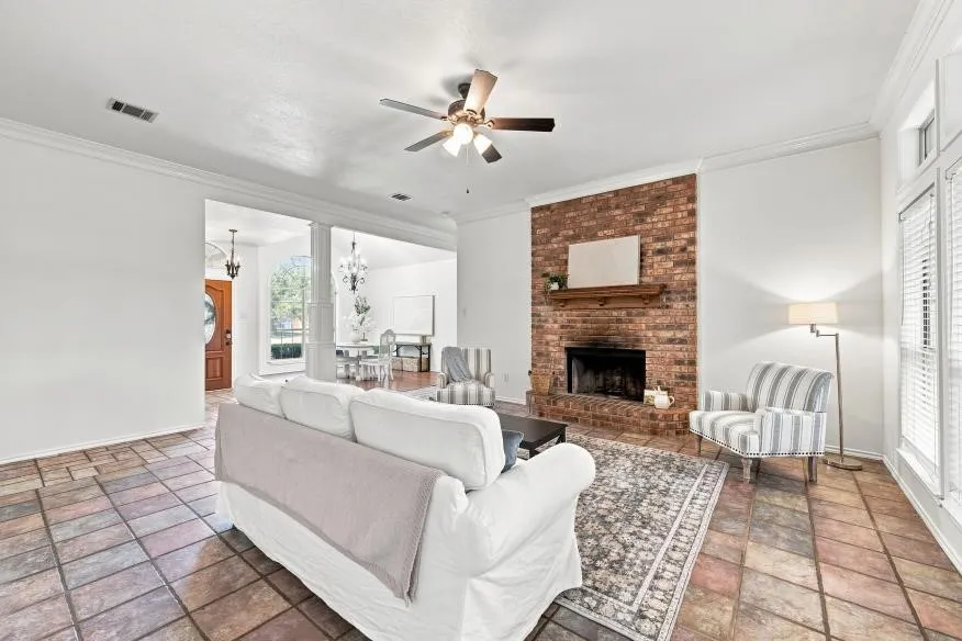 Spacious living area featuring stone tile flooring, a brick fireplace with a wood mantle, and white crown molding