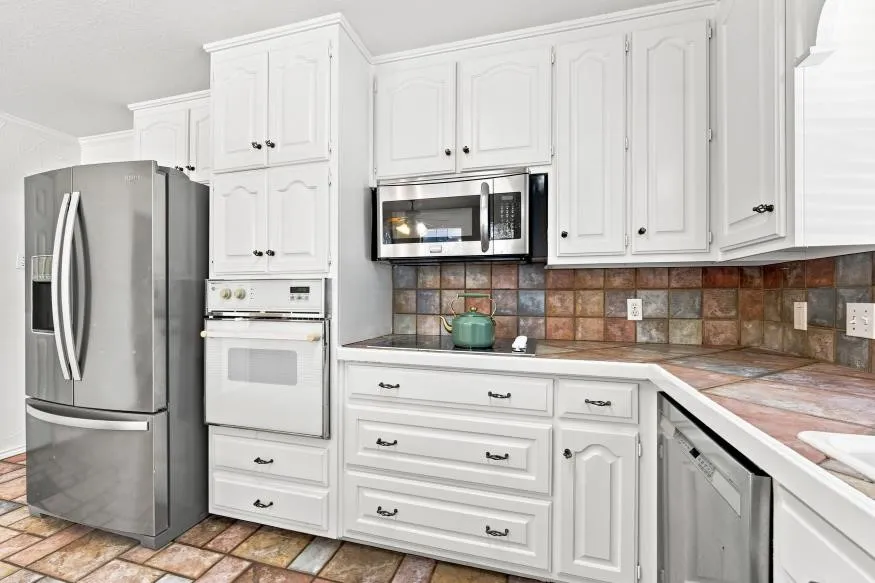 White cabinetry, stainless steel appliances, built-in oven, integrated cooktop, and multi-tone tiled backsplash