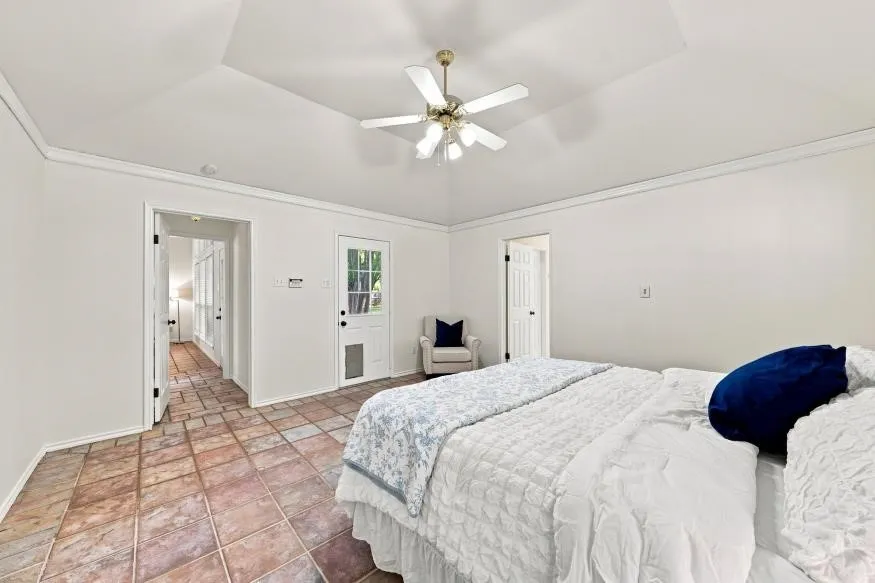Vaulted ceiling with crown molding, ceiling fan, tile flooring, and exterior door with glass panes