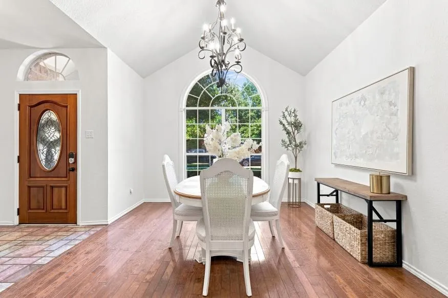 Vaulted ceiling with an ornate chandelier, arched window, wood-finish flooring, and a wood-paneled front door with an oval glass insert
