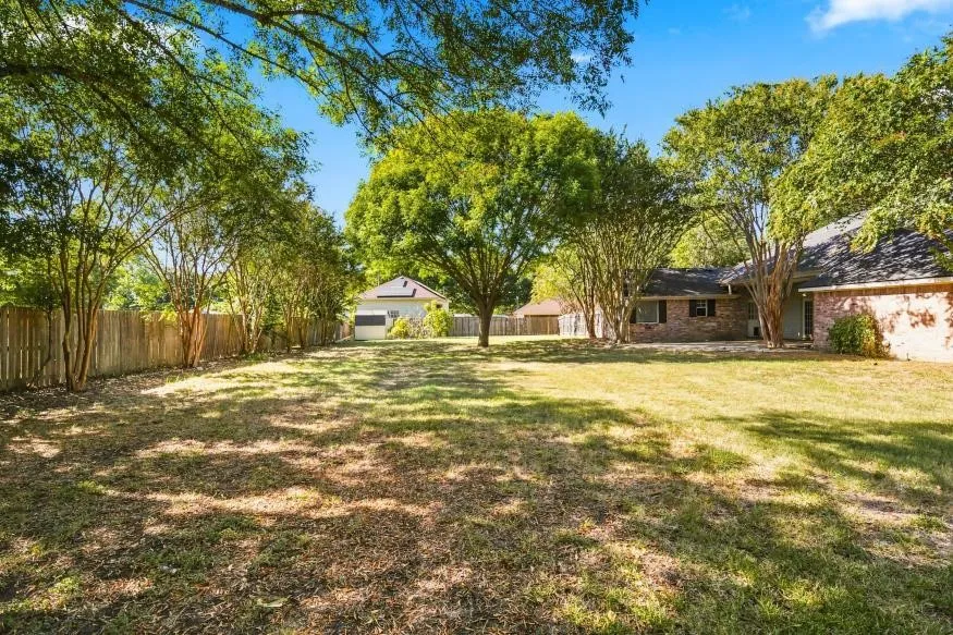 Expansive backyard with a manicured lawn, mature trees, and a wooden privacy fence