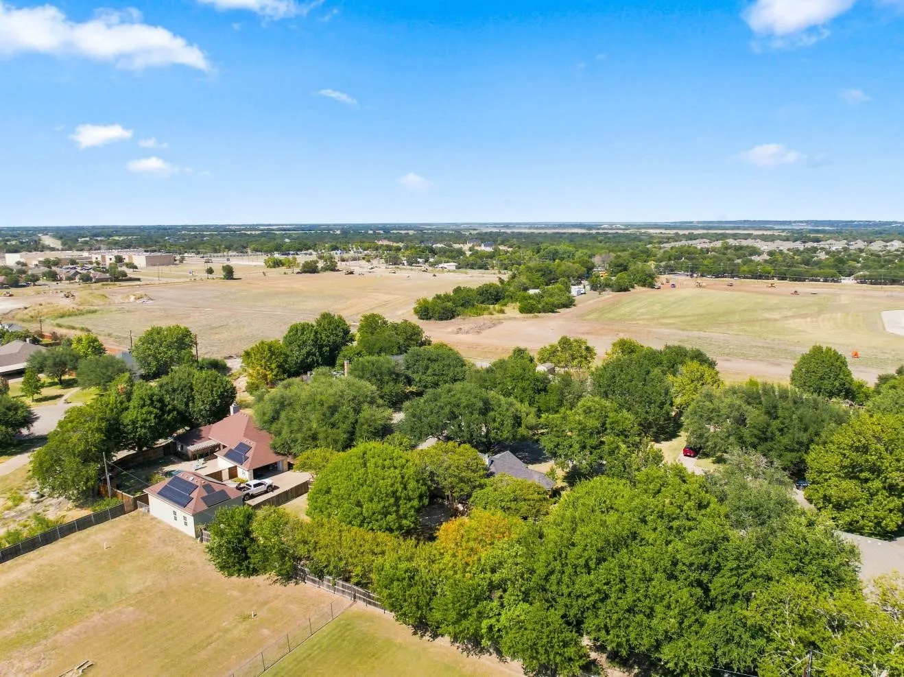 Expansive property featuring a residence with a brown shingle roof, solar panels, and surrounding mature trees