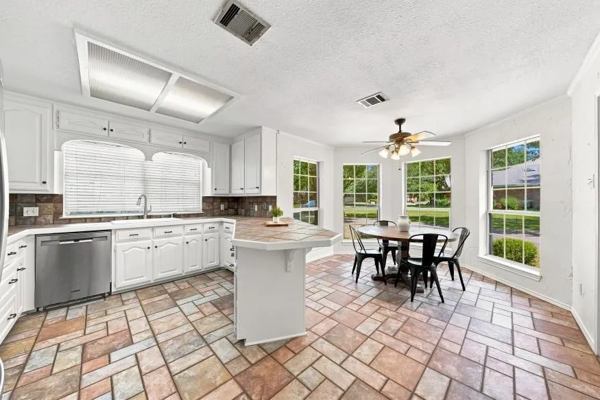 White cabinetry with dark hardware, stainless steel dishwasher, dual basin sink, integrated island with counter seating, and multi-tone tile flooring