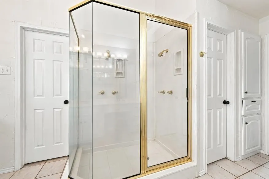 Glass-enclosed shower with gold-tone framing and hardware, integrated shower niche, and tile flooring