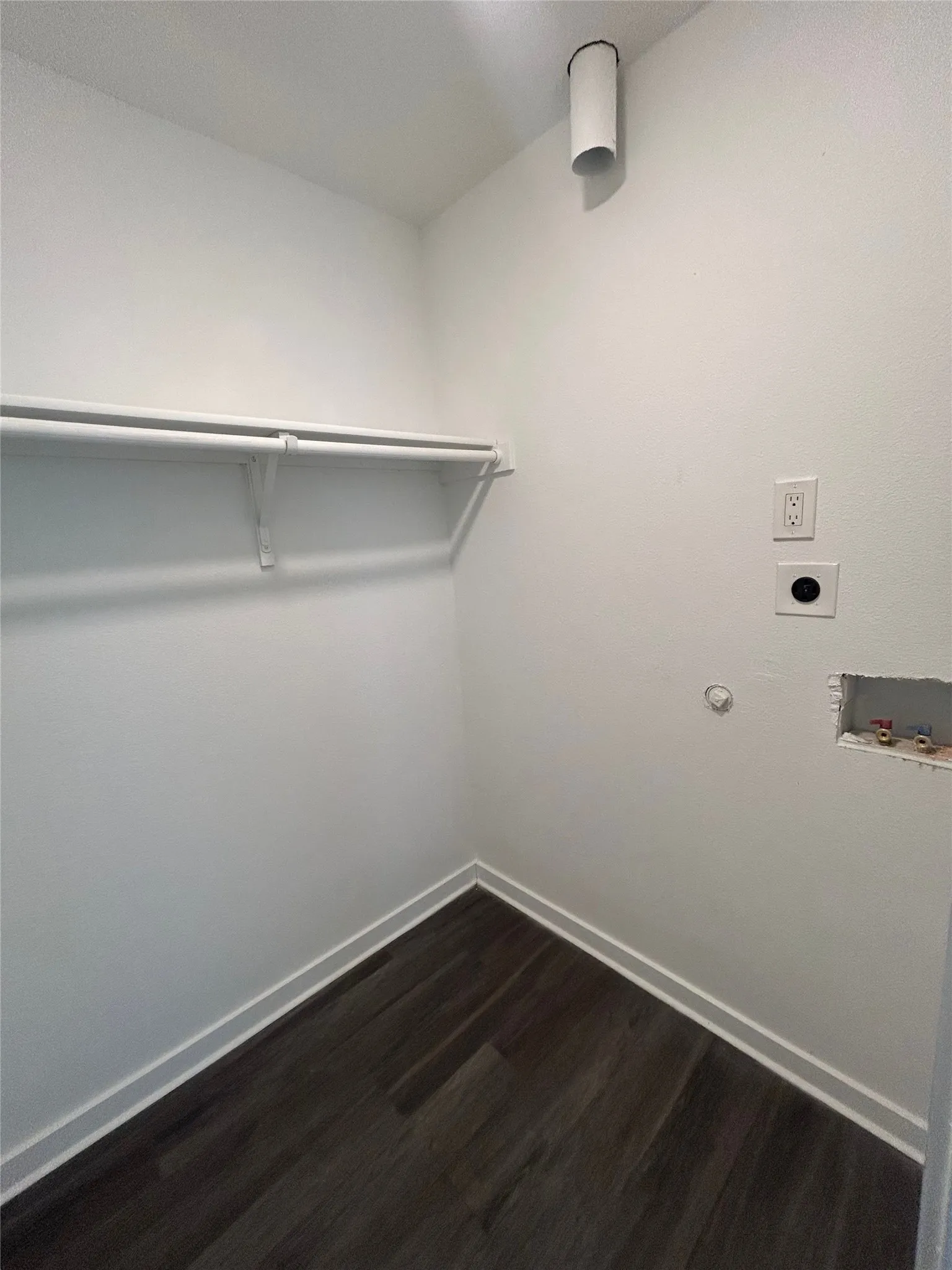Laundry area with wood-finish flooring, white walls, and a built-in hanging rod
