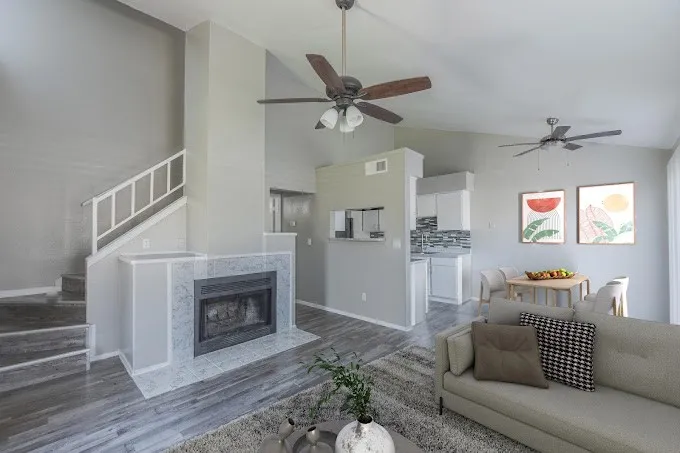 Vaulted ceilings, wood-finish flooring, tiled fireplace, white kitchen cabinetry, and ceiling fans