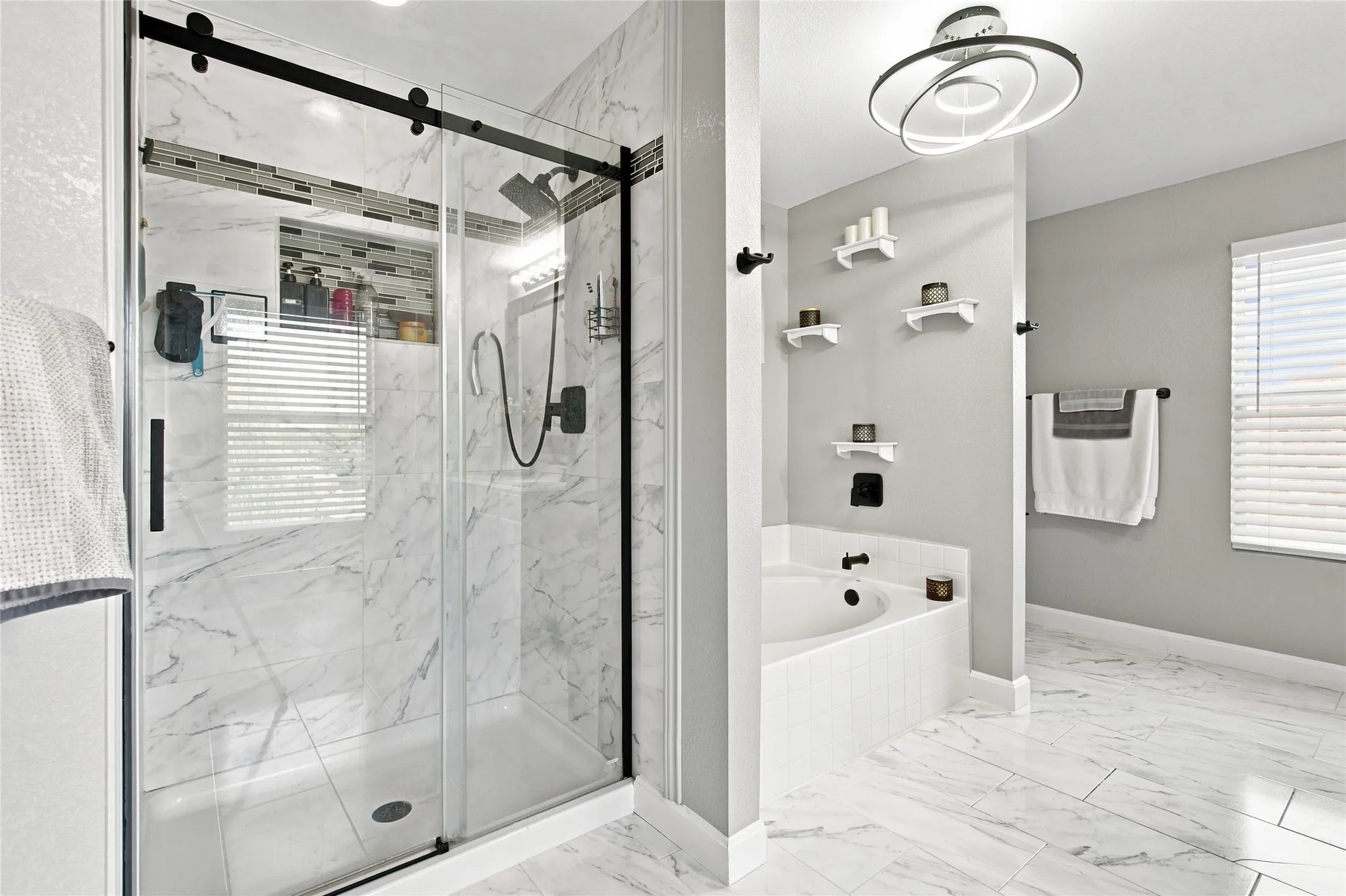 Modern bathroom featuring a glass-enclosed shower with matte black hardware, a corner soaking tub, and white marble-look tile flooring