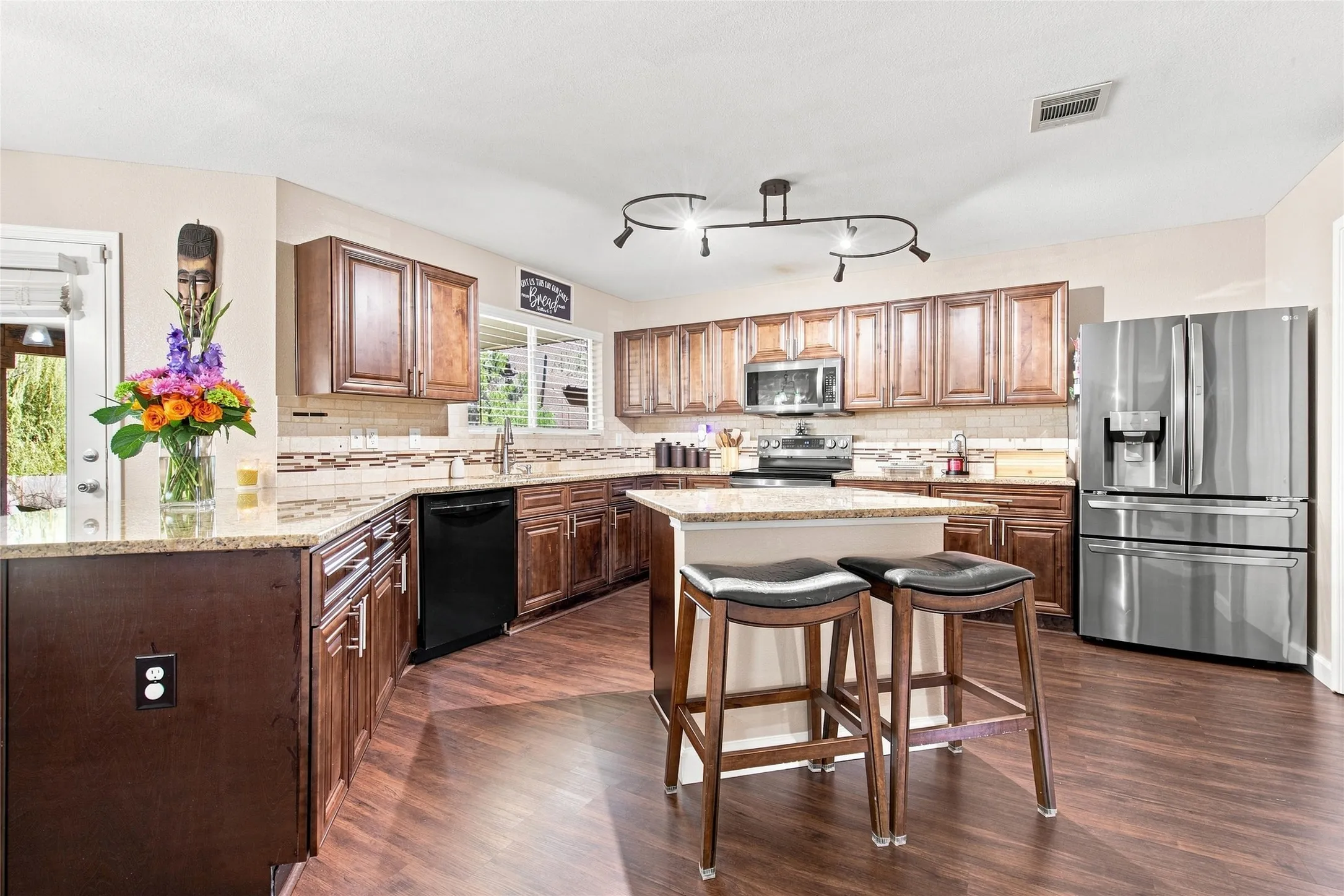 Kitchen featuring wood-finish flooring, dark wood cabinetry, light-toned countertops, a central island, and stainless steel appliances