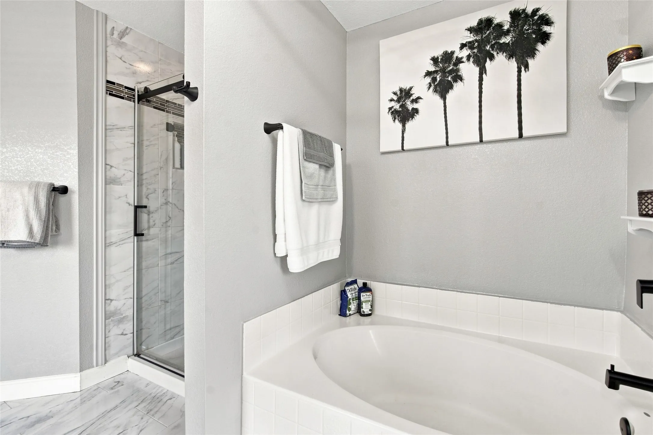 Step-in shower with clear glass enclosure, white ceramic tile bath surround, and black fixtures