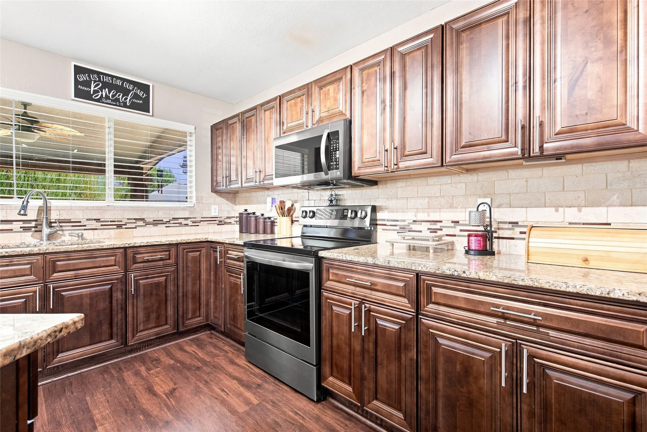 Wood-finish flooring with rich wood cabinetry, stone countertops, and a tiled backsplash