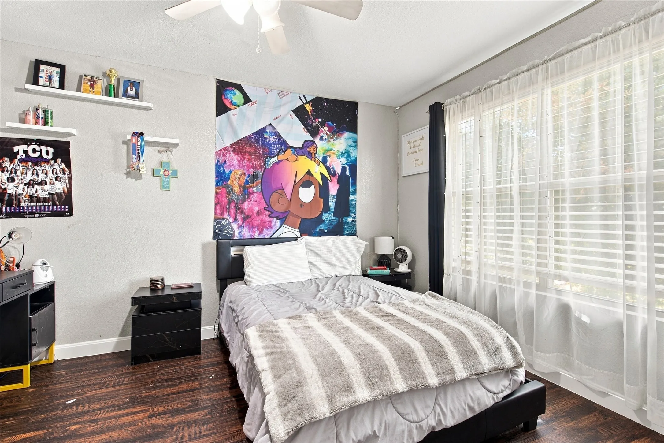 Wood-finish flooring, ceiling fan, window with blinds, and floating wall shelves