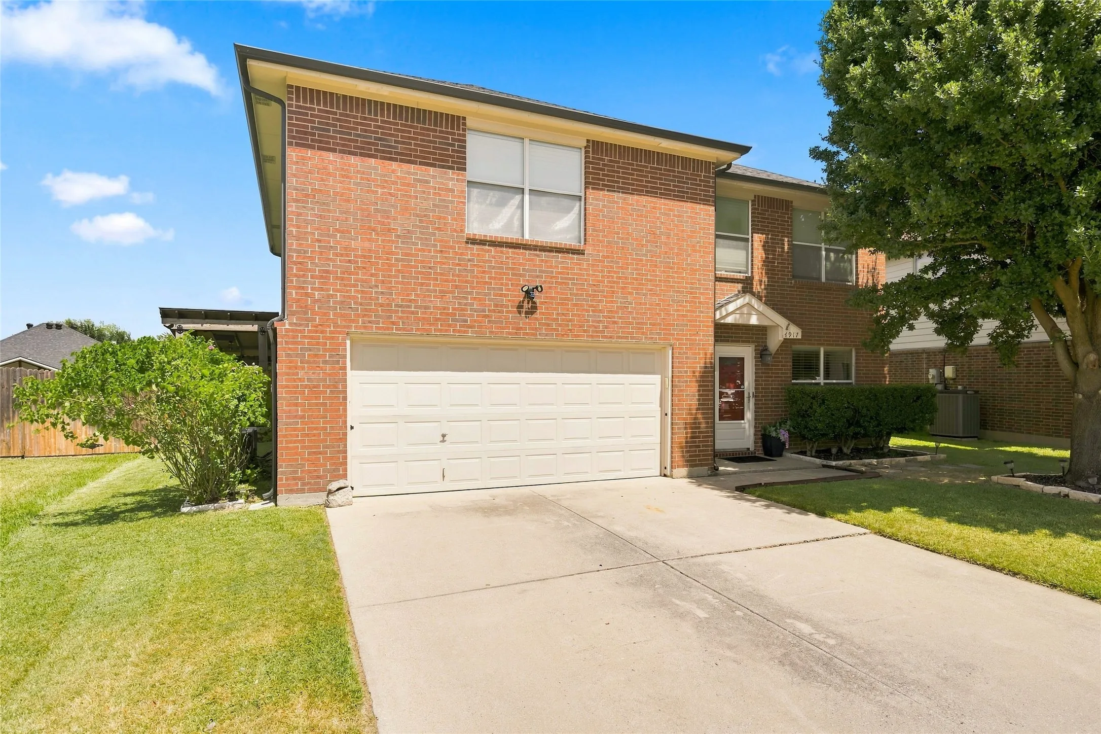 Brick facade, attached garage, concrete driveway, mature tree, established landscaping