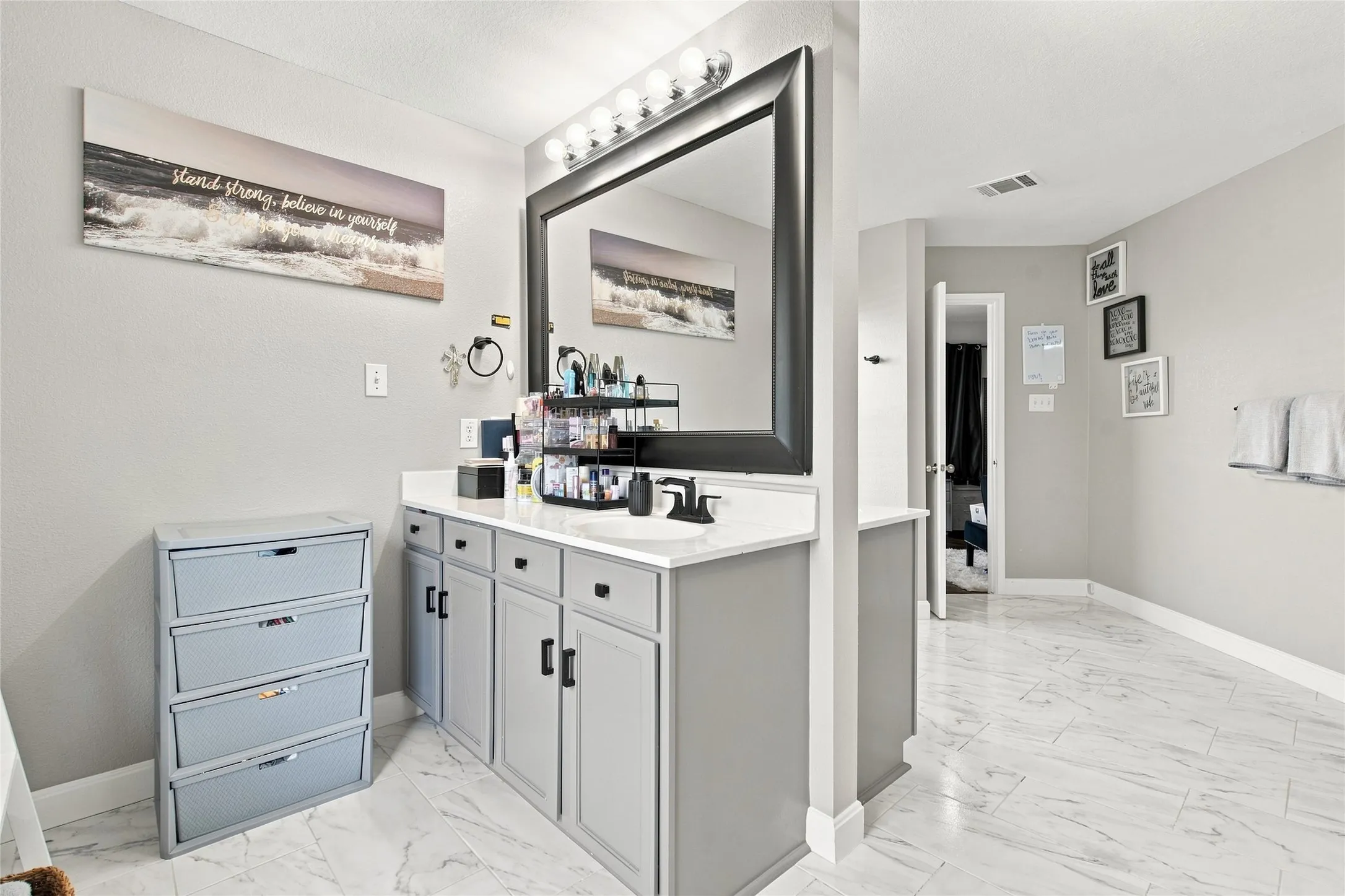 Vanity with a white countertop and undermount sink, large framed mirror with overhead lighting, gray base cabinetry, and tiled flooring