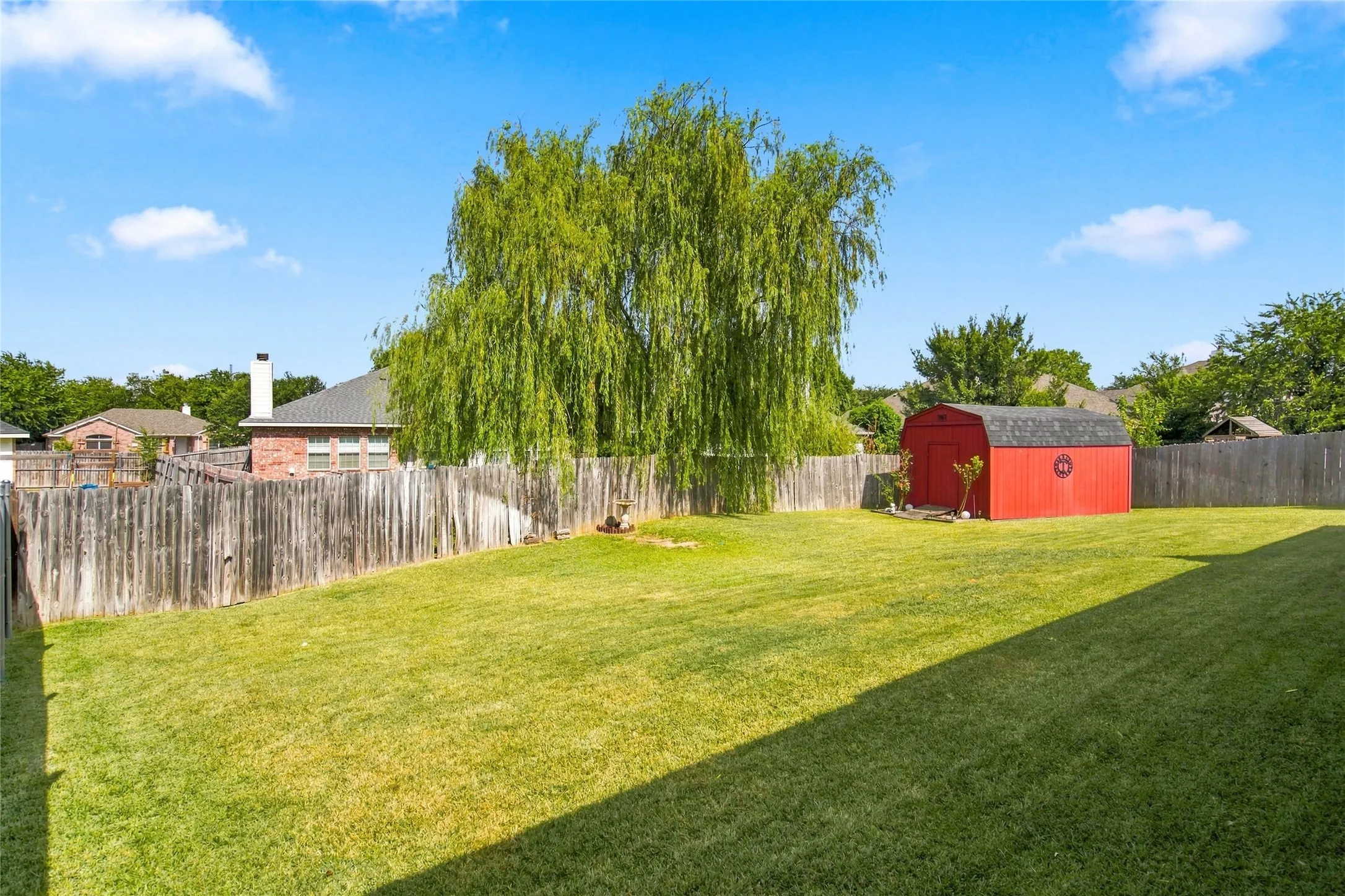 Expansive backyard featuring a manicured lawn, mature trees, and a red storage shed with a shingled roof