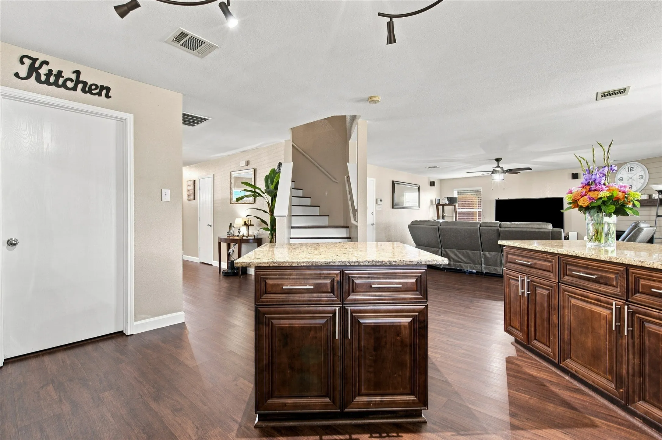 Wood-finish flooring throughout, two kitchen islands with granite countertops, rich wood cabinetry, and track lighting