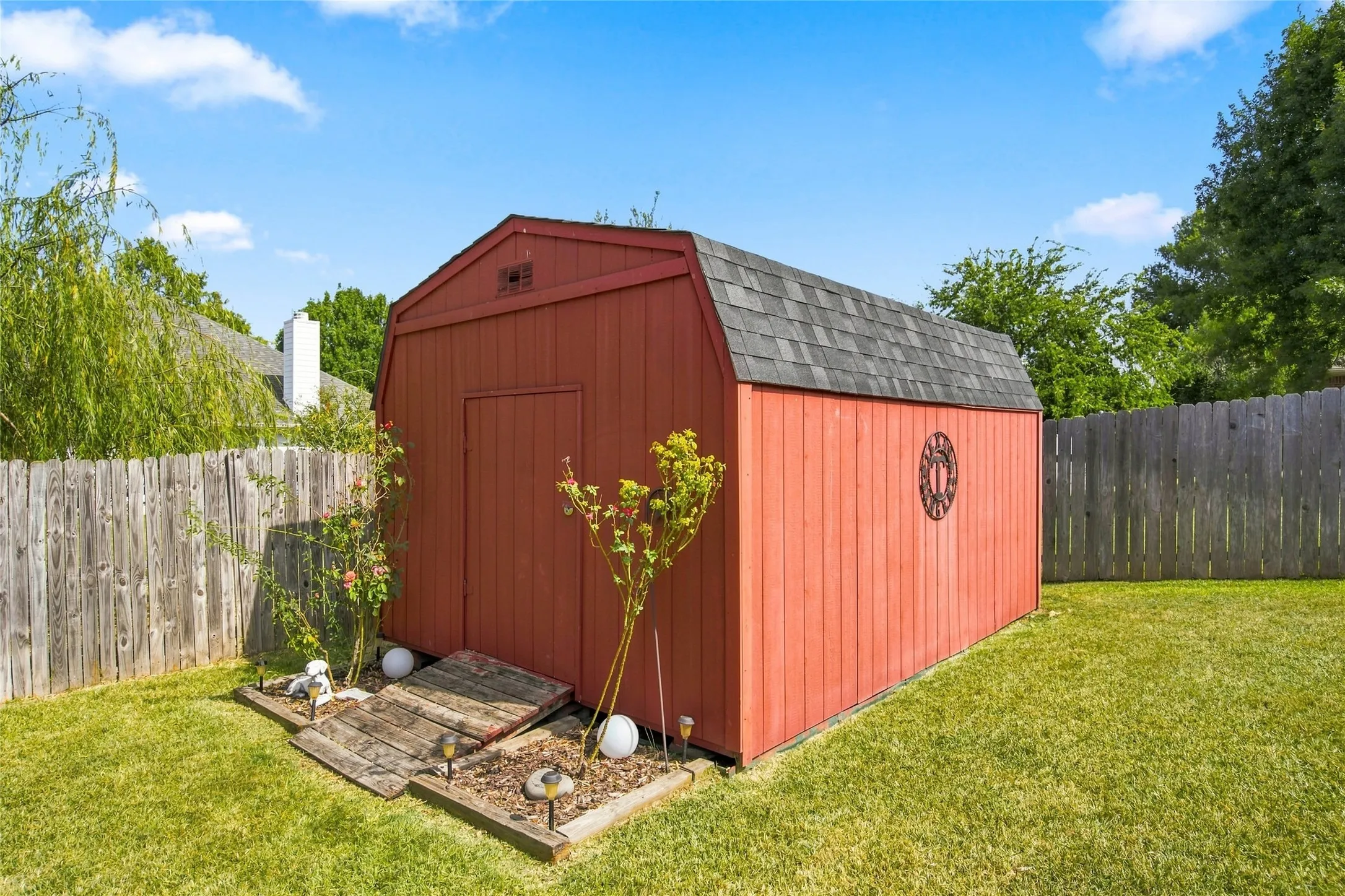 Red wood-paneled storage shed with a gambrel roof and shingle siding