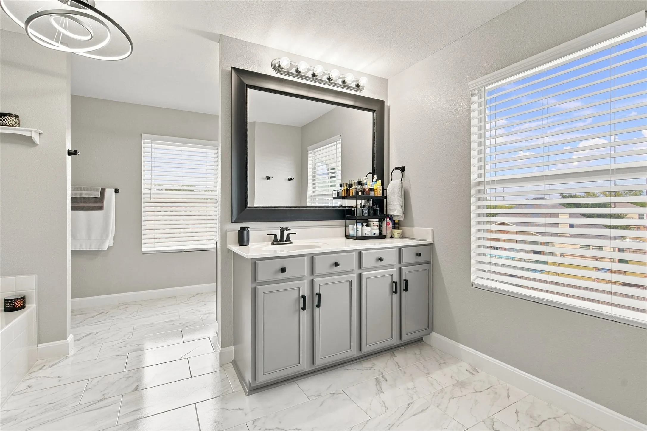 Bathroom featuring a single vanity with gray cabinetry, white countertop, and a large framed mirror