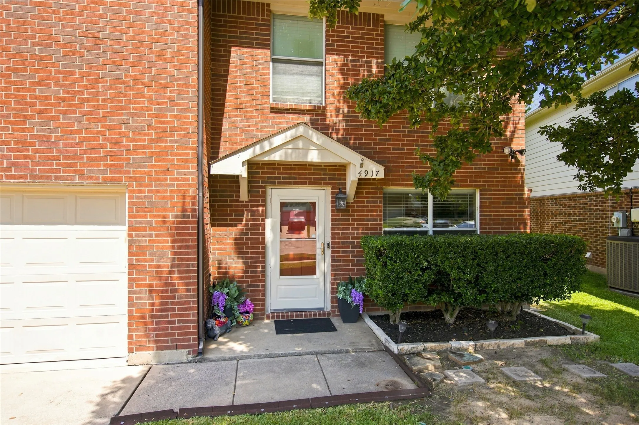 Brick exterior with a covered entry, white garage door, and established front landscaping