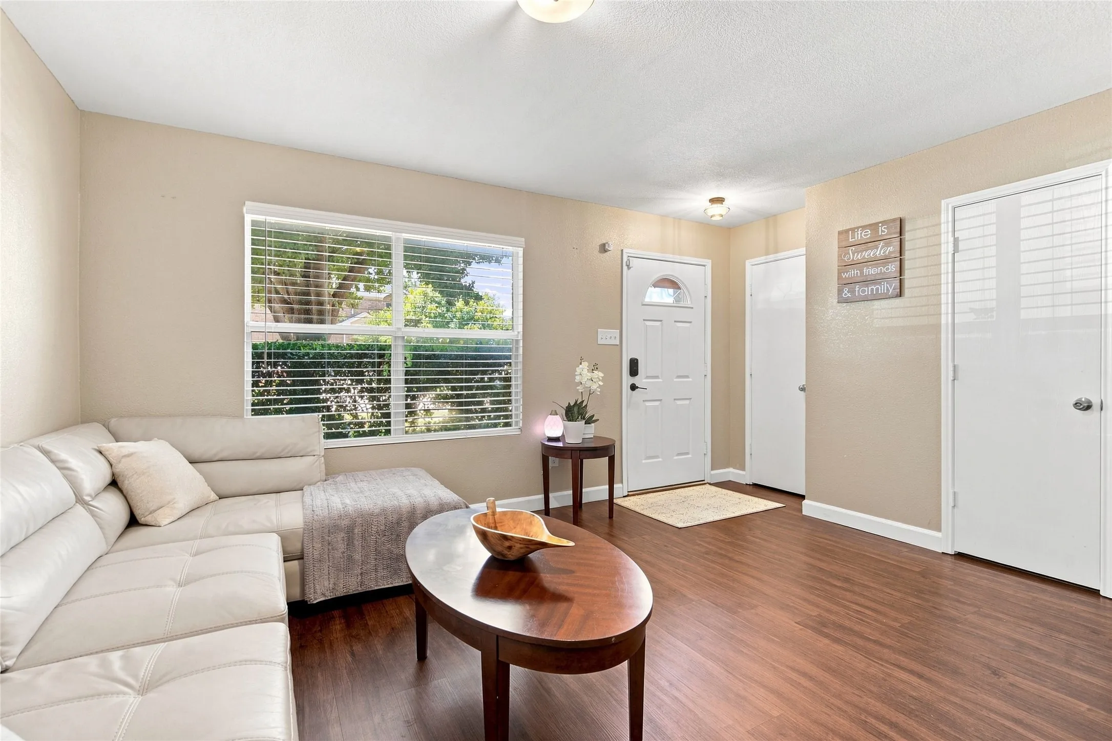 Wood-finish flooring throughout, multiple windows with blinds, a white paneled entry door with frosted glass, and white interior doors