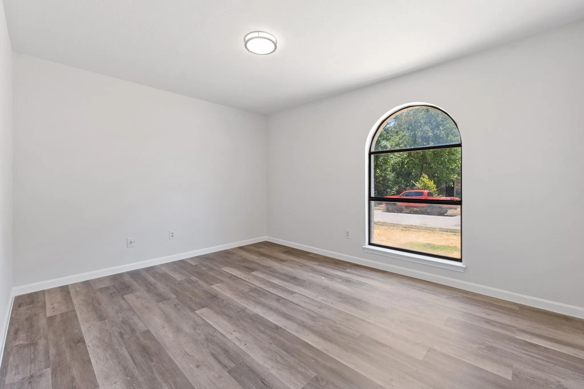 Arch-top window with black frame, wood-finish flooring, recessed lighting, and white walls