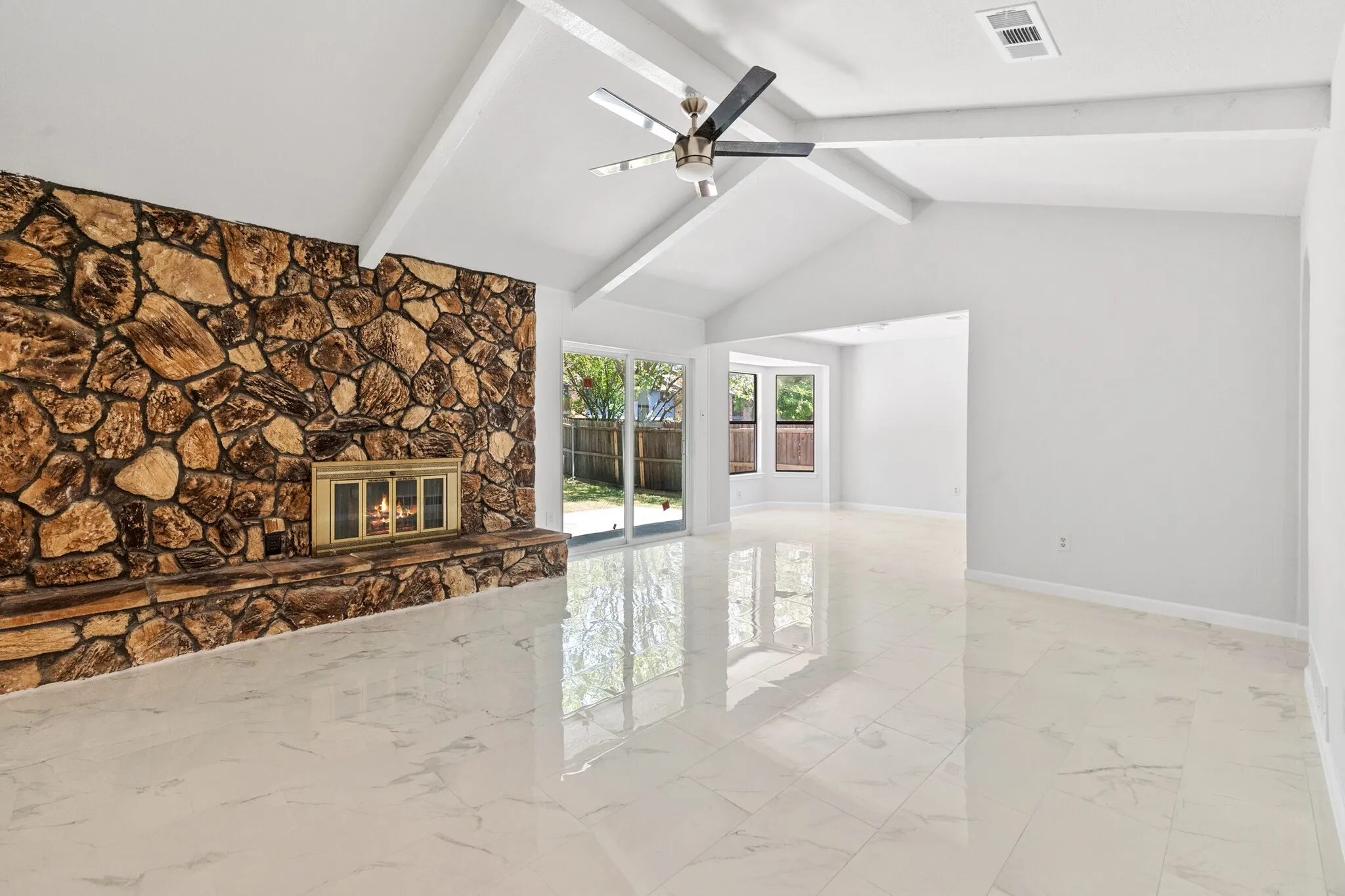 Vaulted ceiling, stone-clad fireplace, large format tile flooring, sliding glass door, and ceiling fan