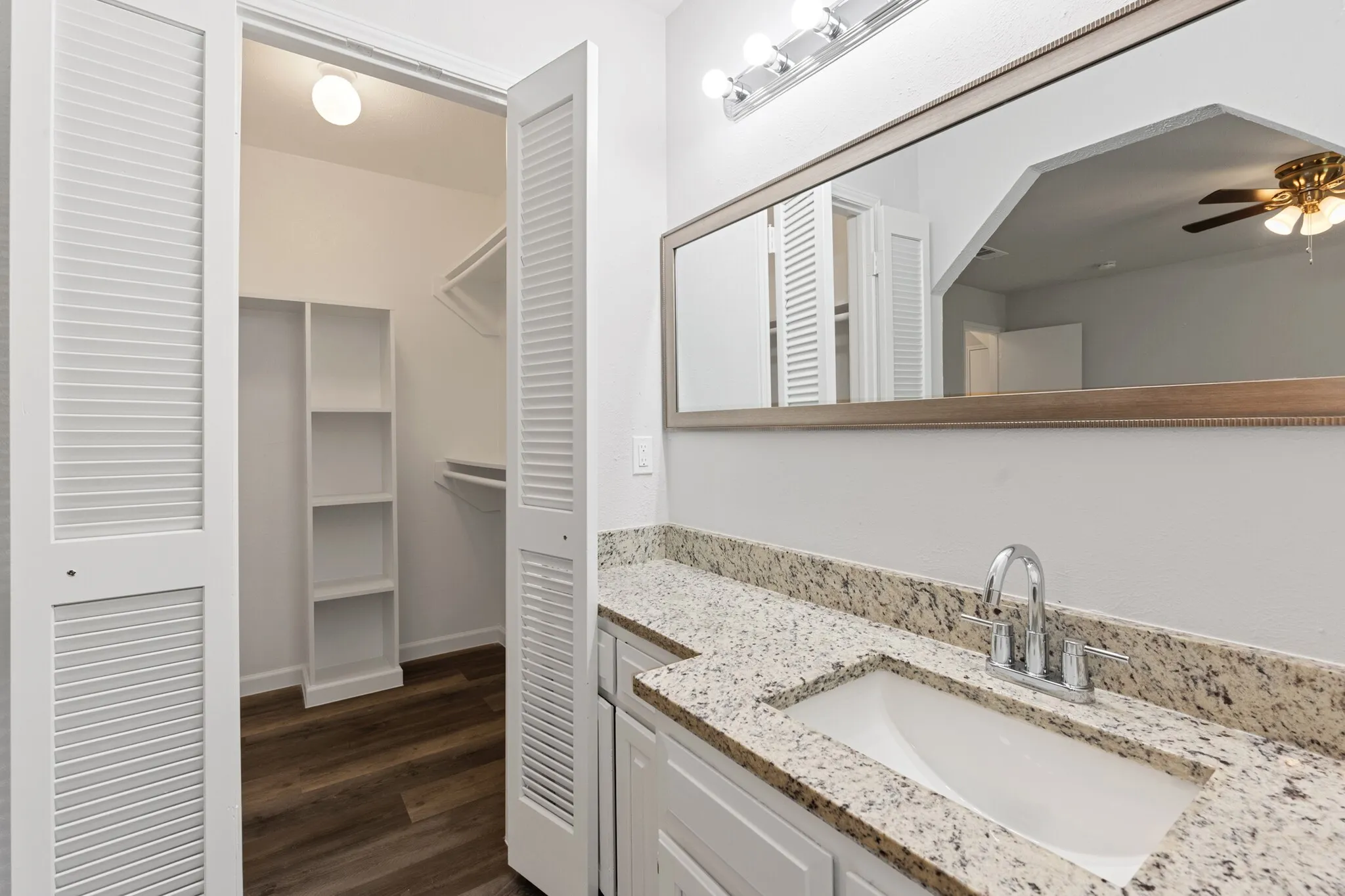 Louvered bifold doors, built-in closet shelving, double vanity with integrated sinks, chrome fixtures, and speckled stone countertops