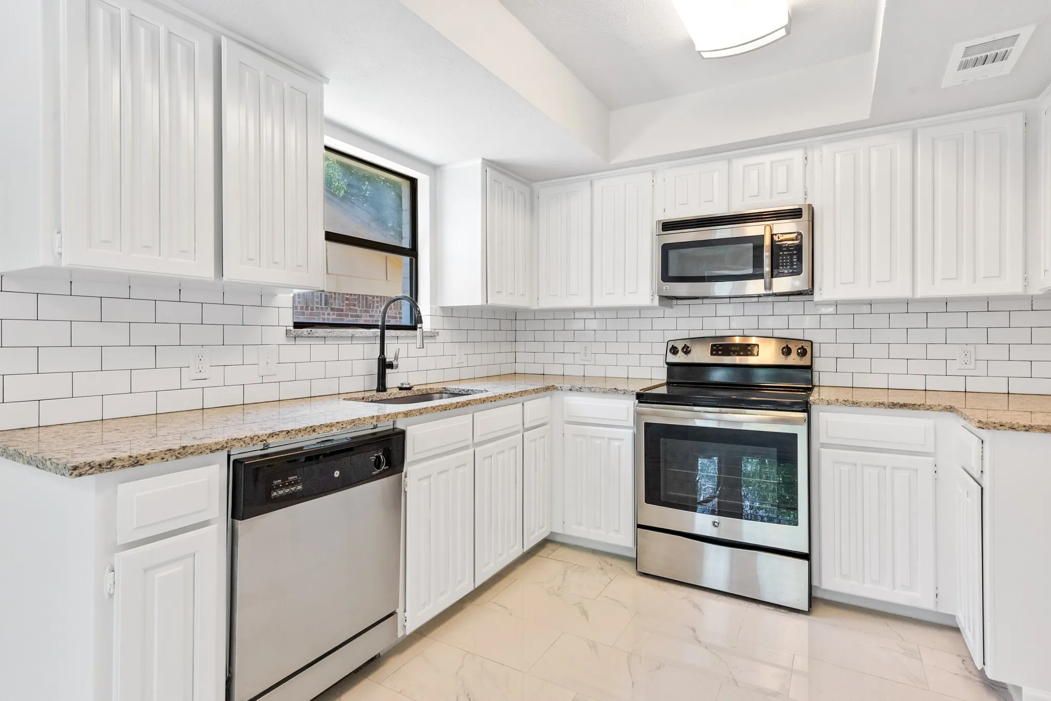 Bright kitchen featuring white cabinetry, subway tile backsplash, granite countertops, stainless steel appliances, and tile flooring