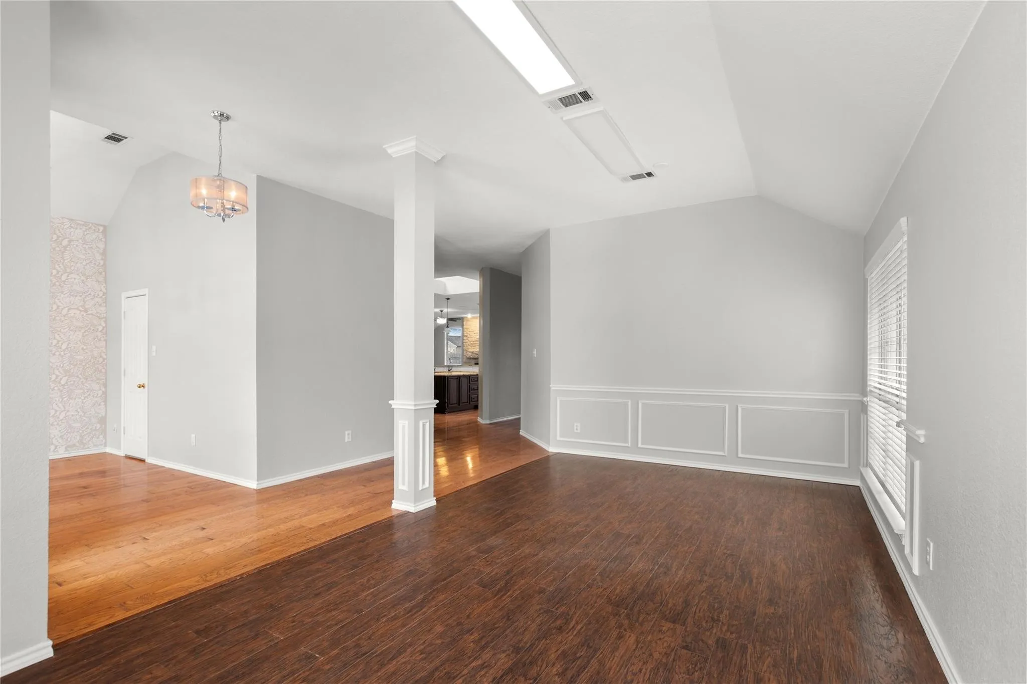 Spacious upper-level room featuring gleaming wood-finish flooring, crisp white walls with wainscoting detail, recessed lighting, and a pendant fixture