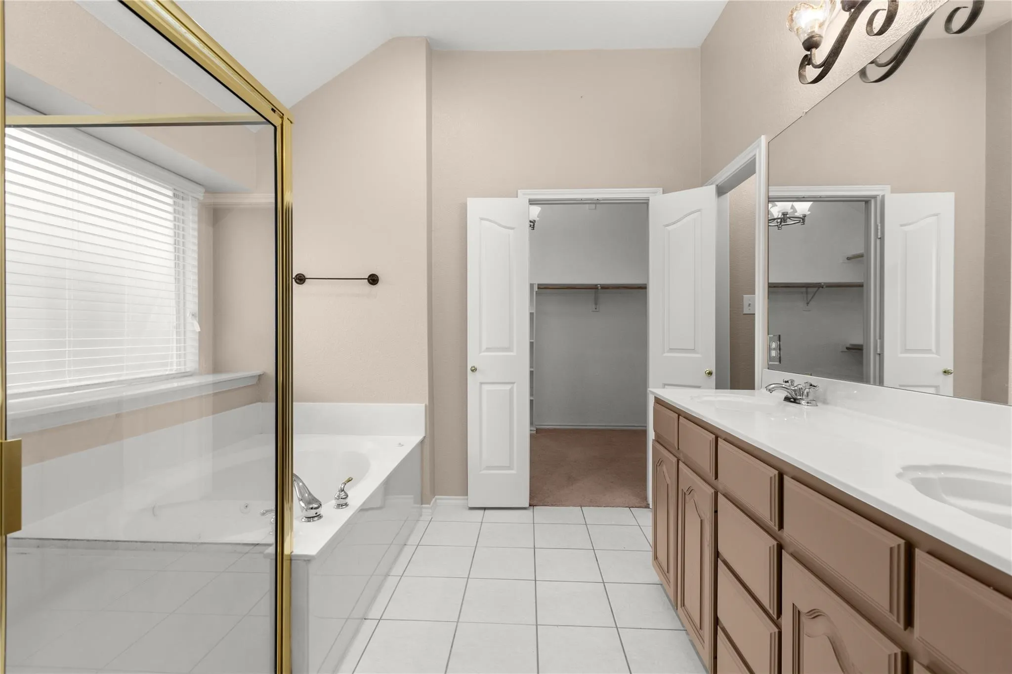 Bathroom featuring a dual vanity with integrated sinks, a built-in tub, a shower enclosure with a brass frame, and tile flooring
