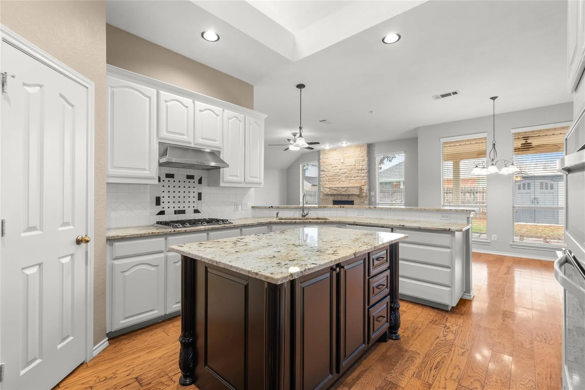 Kitchen featuring a two-tier island with granite countertops, white cabinetry, and wood-finish flooring