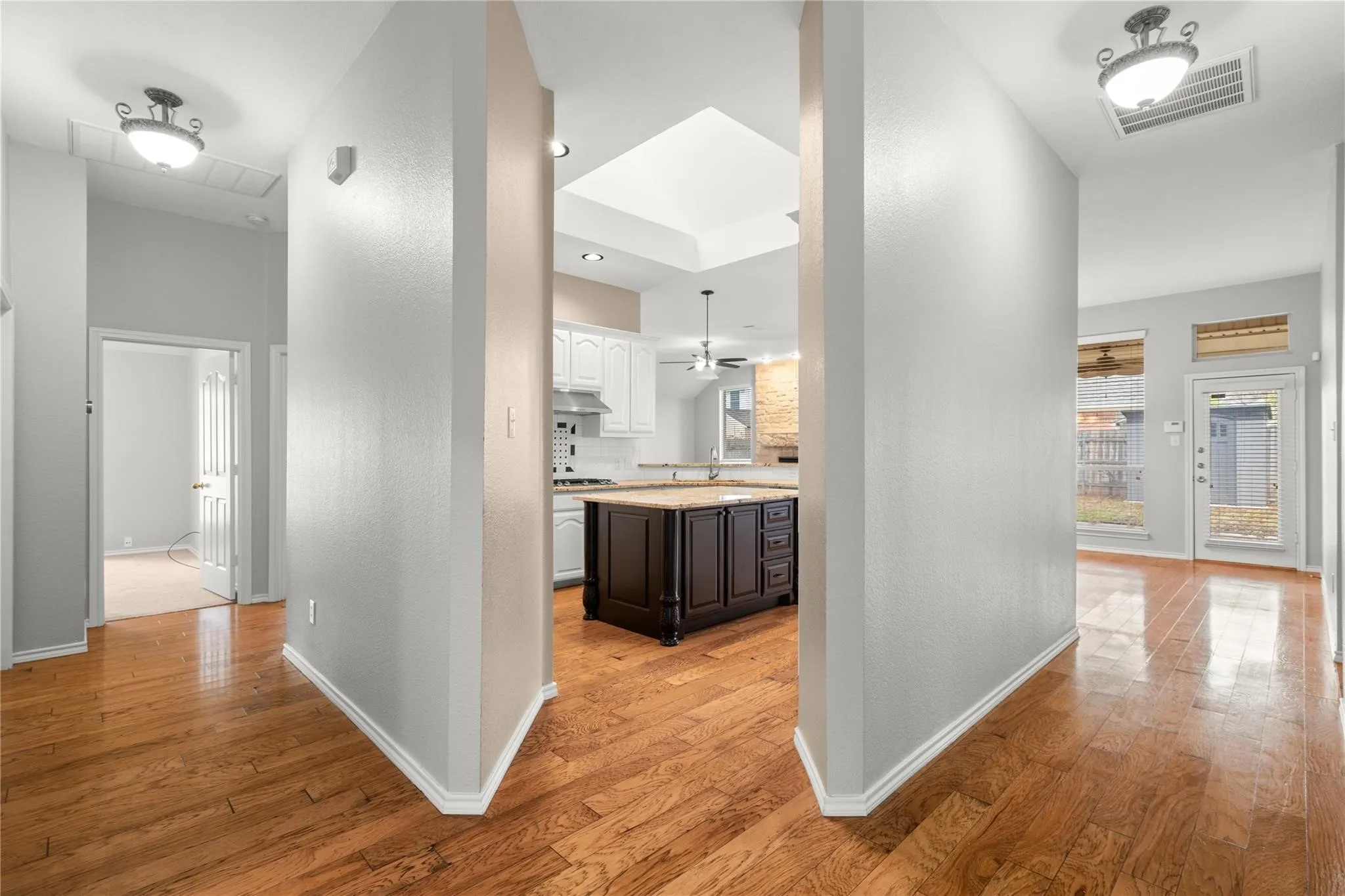 Wood-finish flooring throughout, a kitchen featuring white cabinetry and a dark island, stainless steel appliances, and a skylight