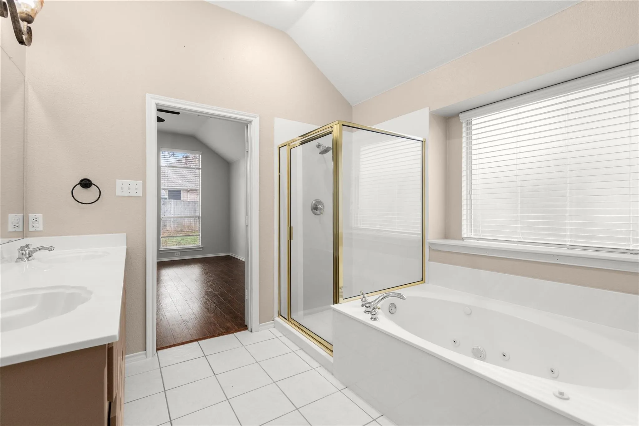 Dual vanity with integrated sinks, a built-in jetted tub, a glass-enclosed shower, vaulted ceilings, and tile flooring