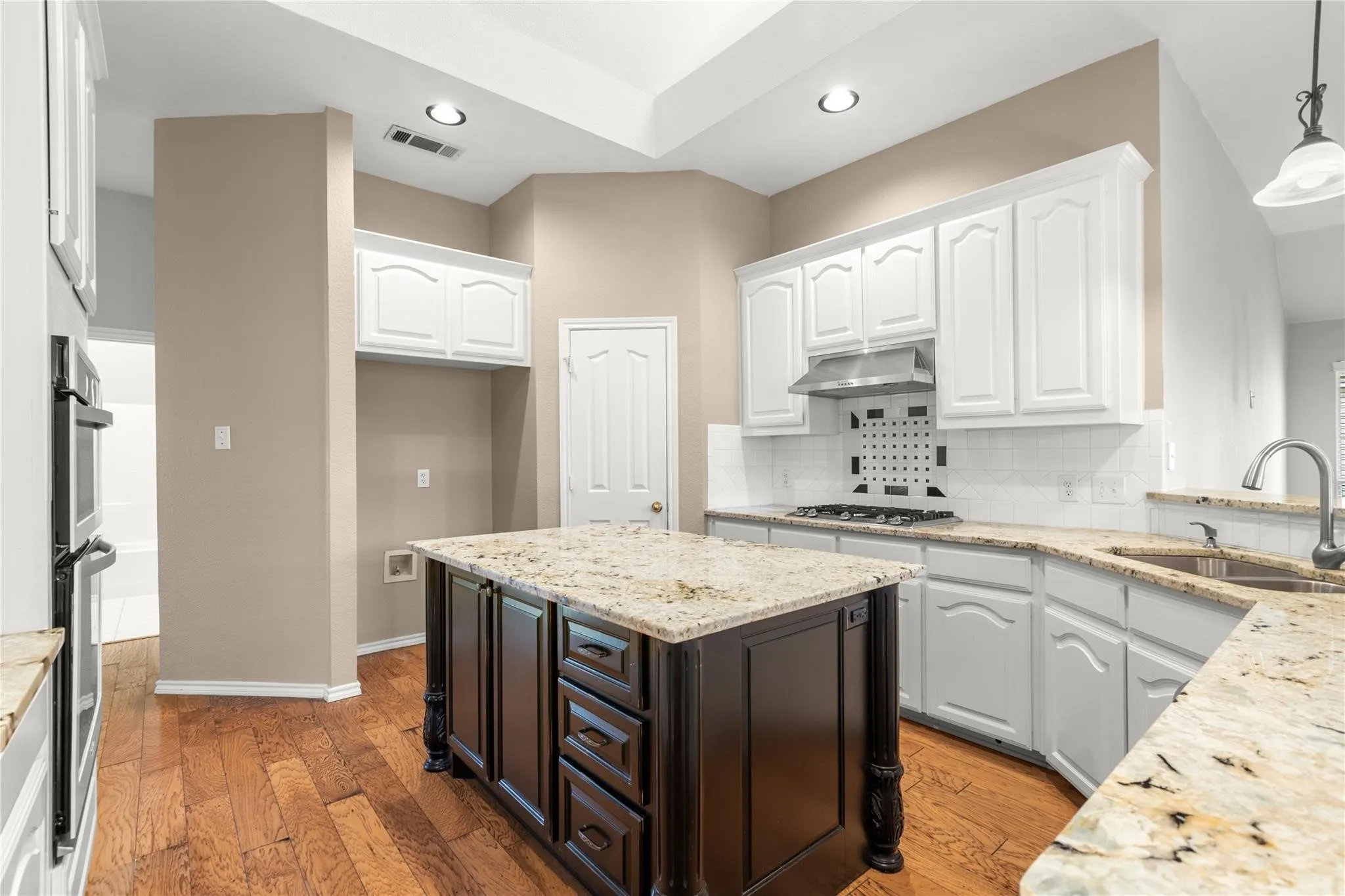Kitchen featuring wood-finish flooring, white cabinetry, an island with dark wood-finish cabinetry, light-toned countertops, and a stainless steel range hood