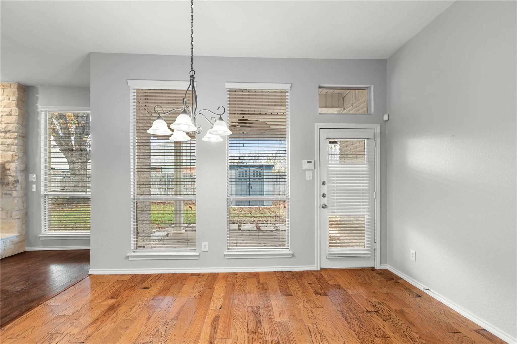 Hardwood flooring, light gray wall finishes, a multi-light chandelier, multiple windows with blinds, and a glass-paneled exterior door