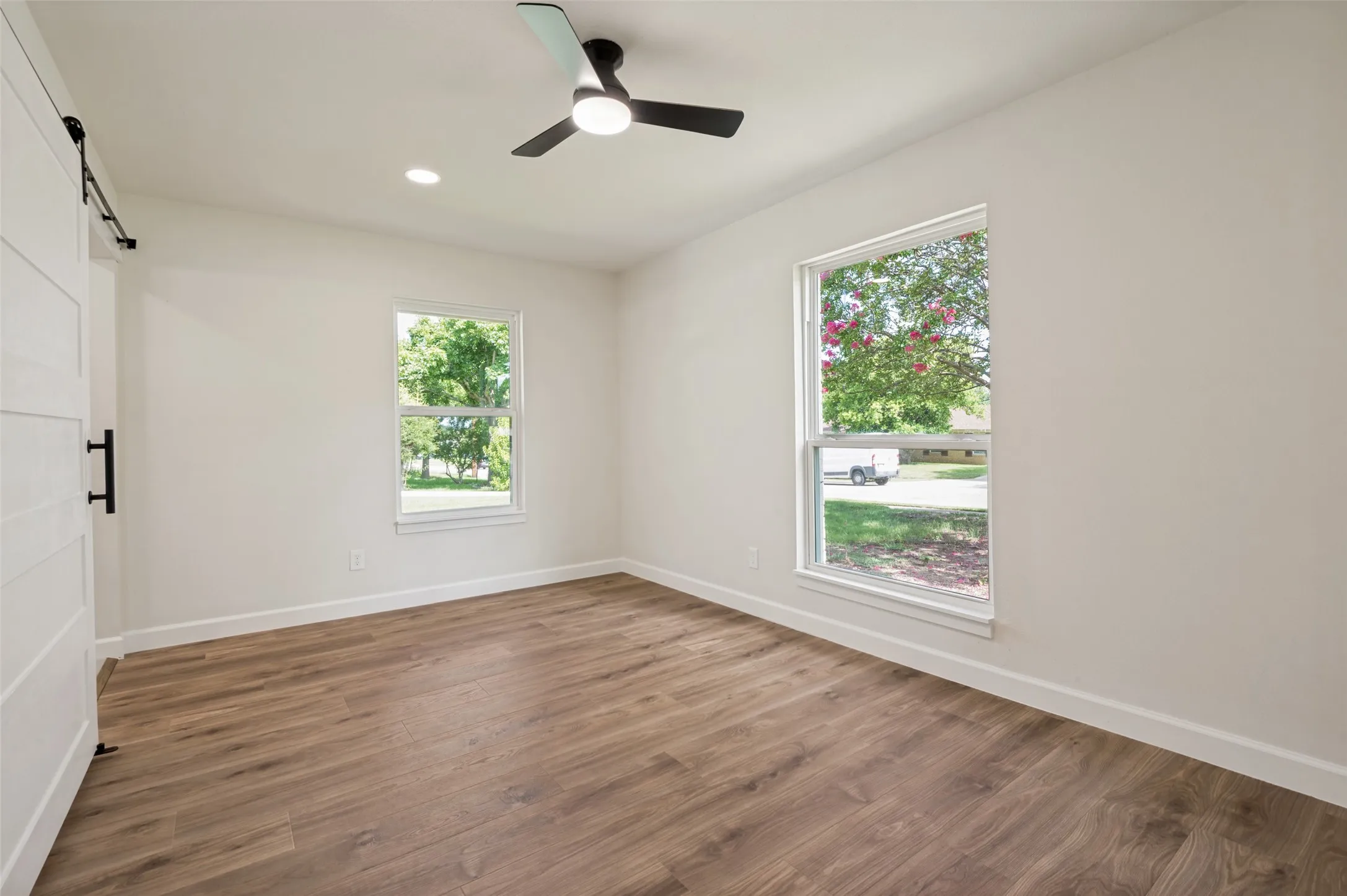 Wood-finish flooring, white walls, two windows, recessed lighting, and a black ceiling fan