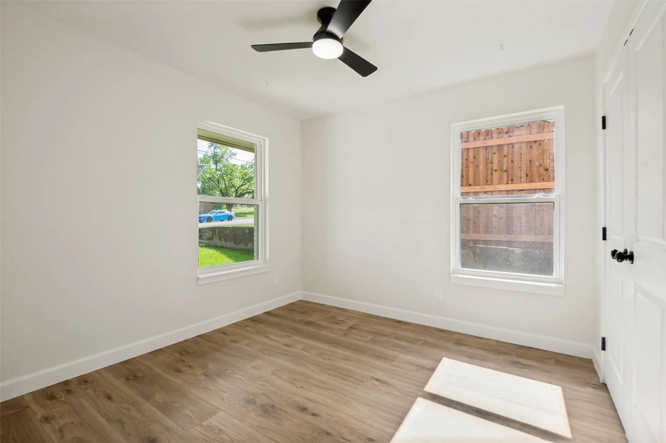 Wood-finish flooring, white walls, two windows, and a ceiling fan with integrated lighting